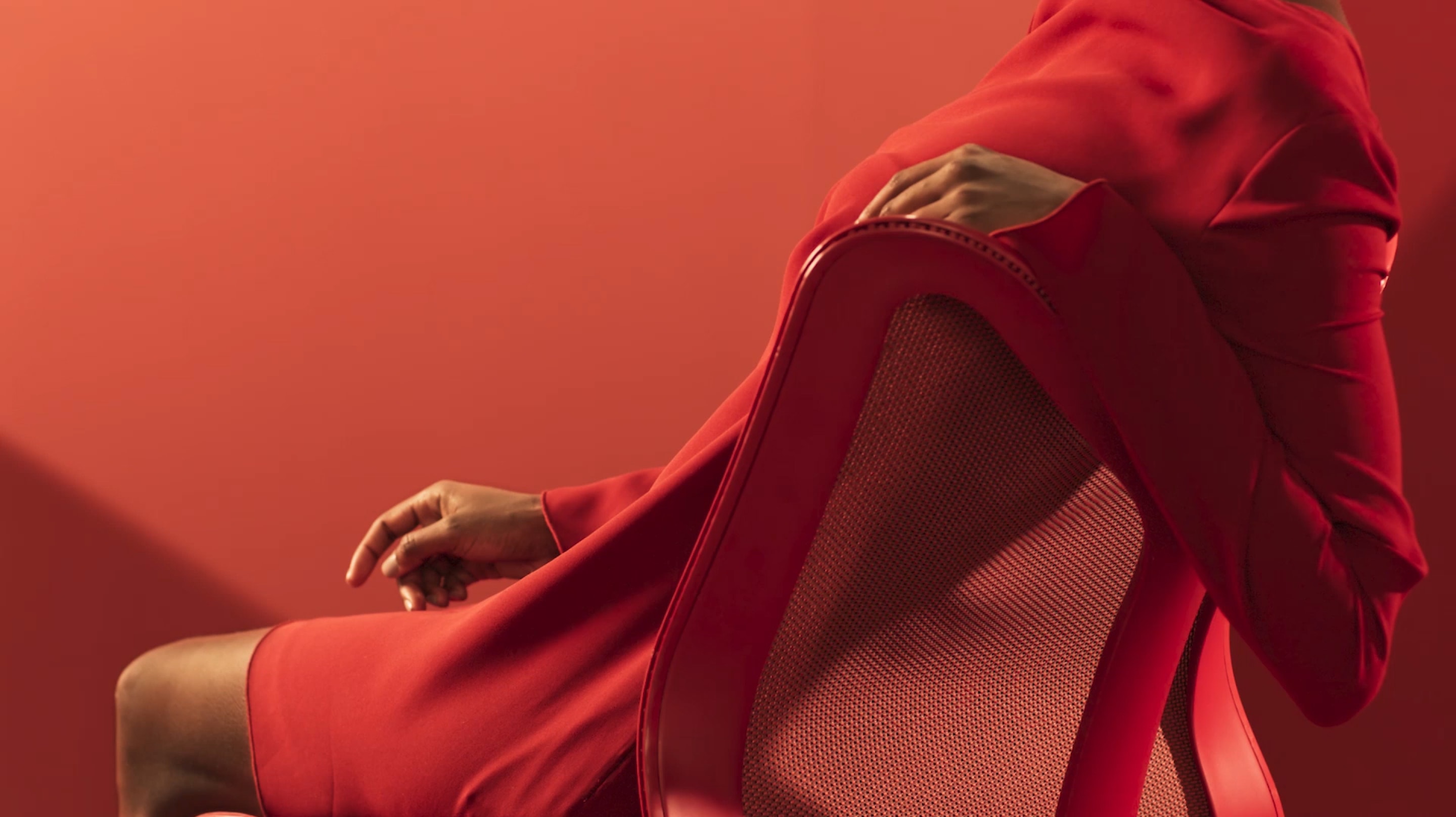 A woman in a red dress reclines with her arm over the backrest of a Canyon red Cosm Chair. Select play button to start video. 
